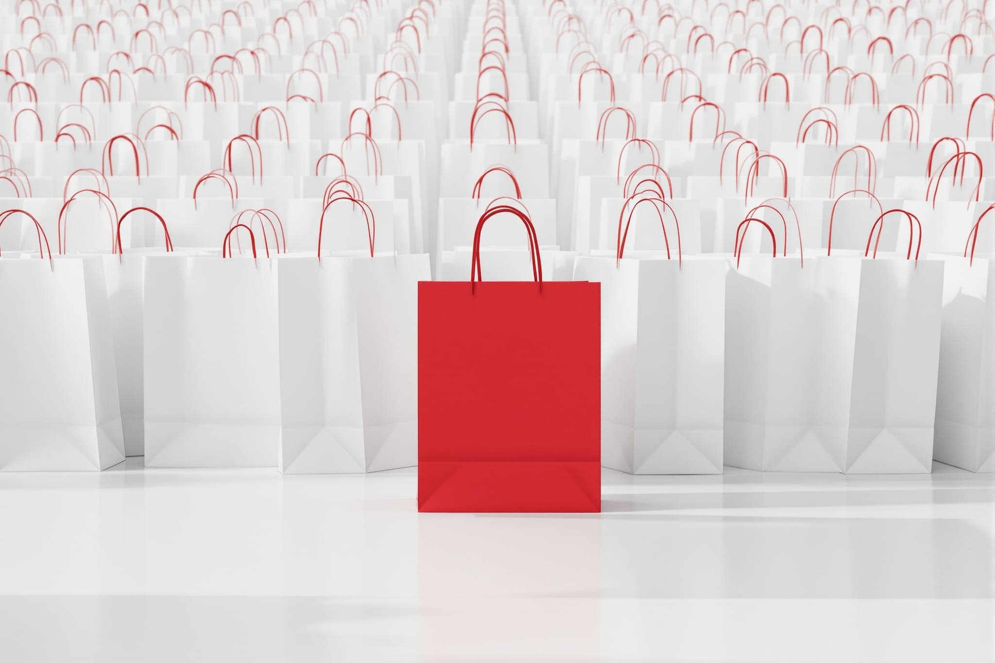 Plain shopping bags in a row on a pale floor, exactly one with crimson handles