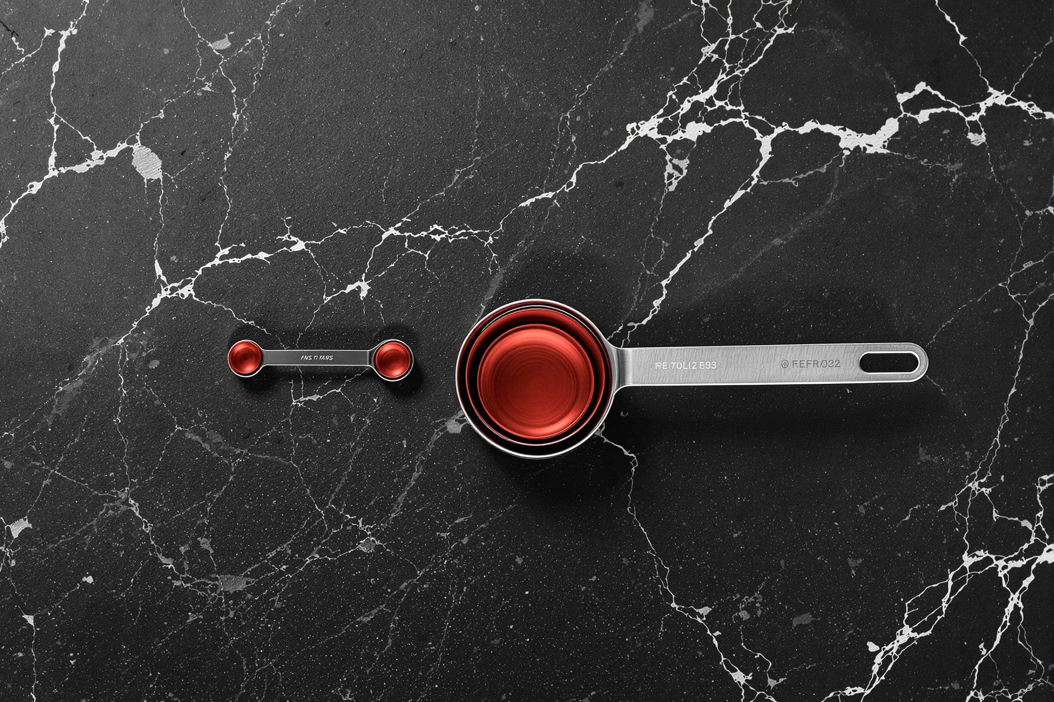 Nested steel measuring cups in a line, the smallest lined crimson