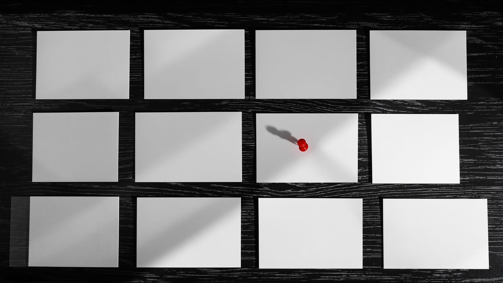 Blank white cards laid out in a grid on a dark desk, a single crimson pushpin on one of them