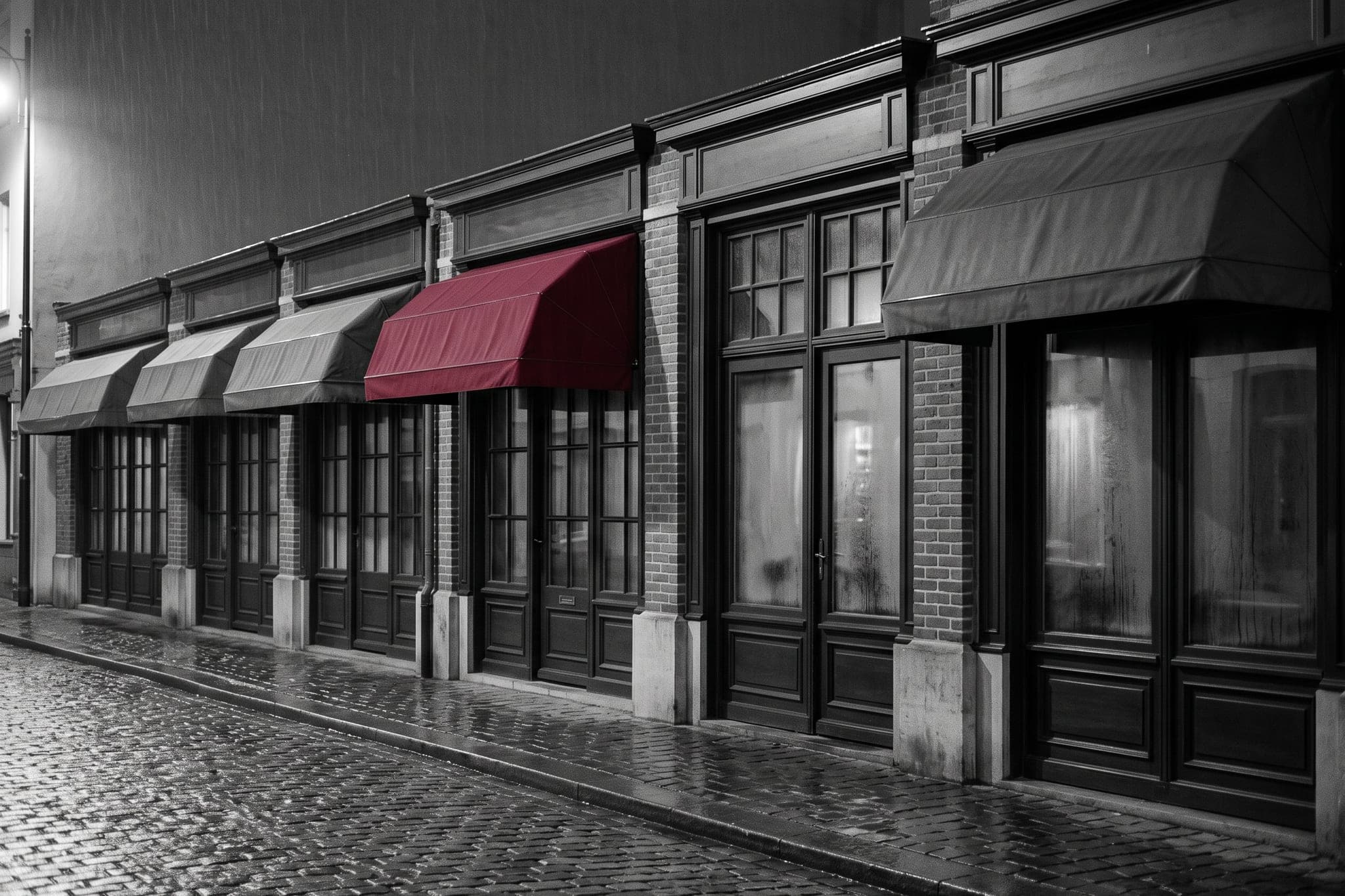 A row of identical shopfronts in the rain, exactly one with a crimson awning