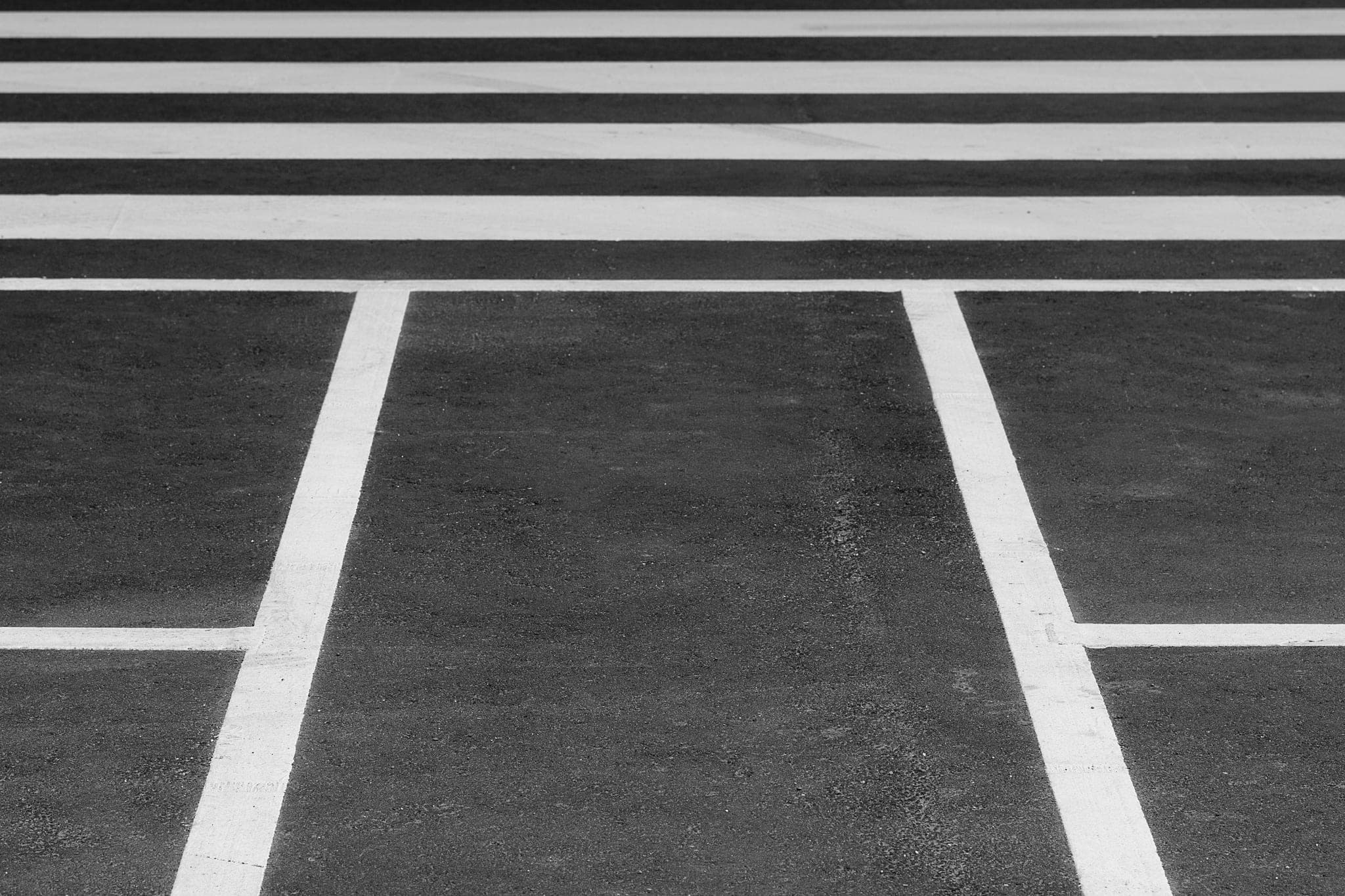 White lines painted on dark asphalt: a pedestrian crossing and the lane markings that meet it