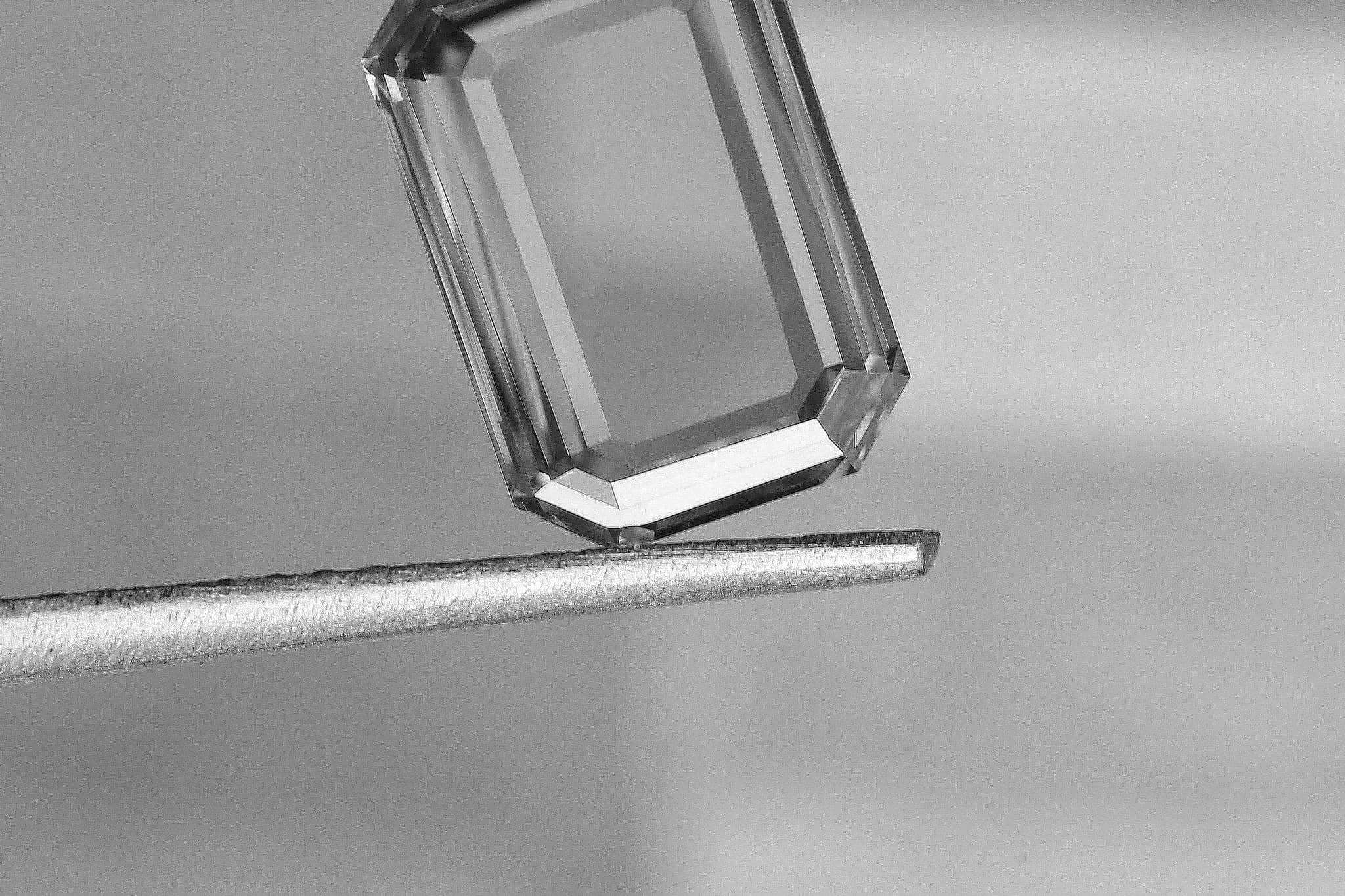 A faceted clear gemstone resting on the tip of a thin metal rod