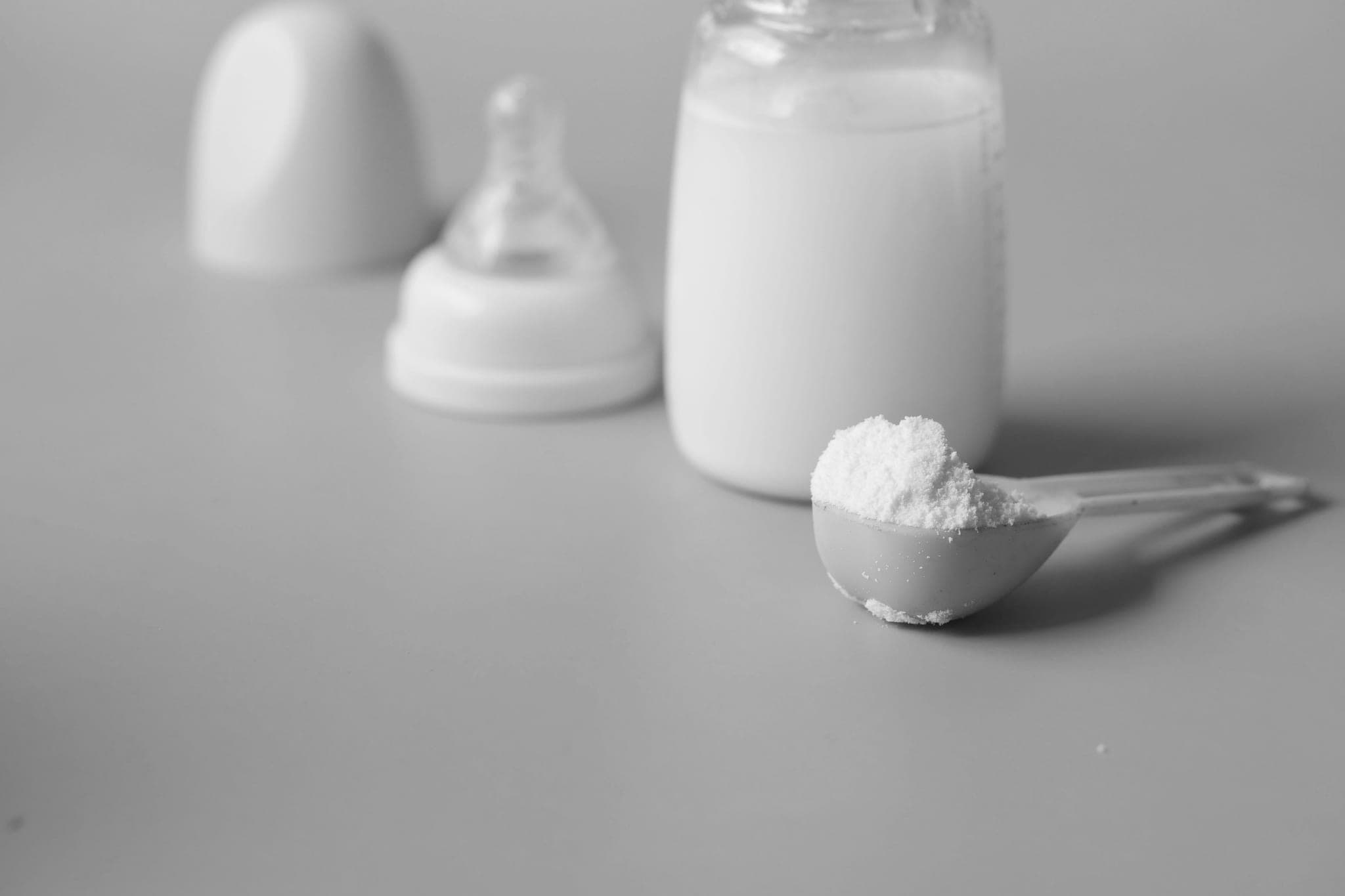 A scoop of formula powder in front of a bottle of milk, its teat and its cap