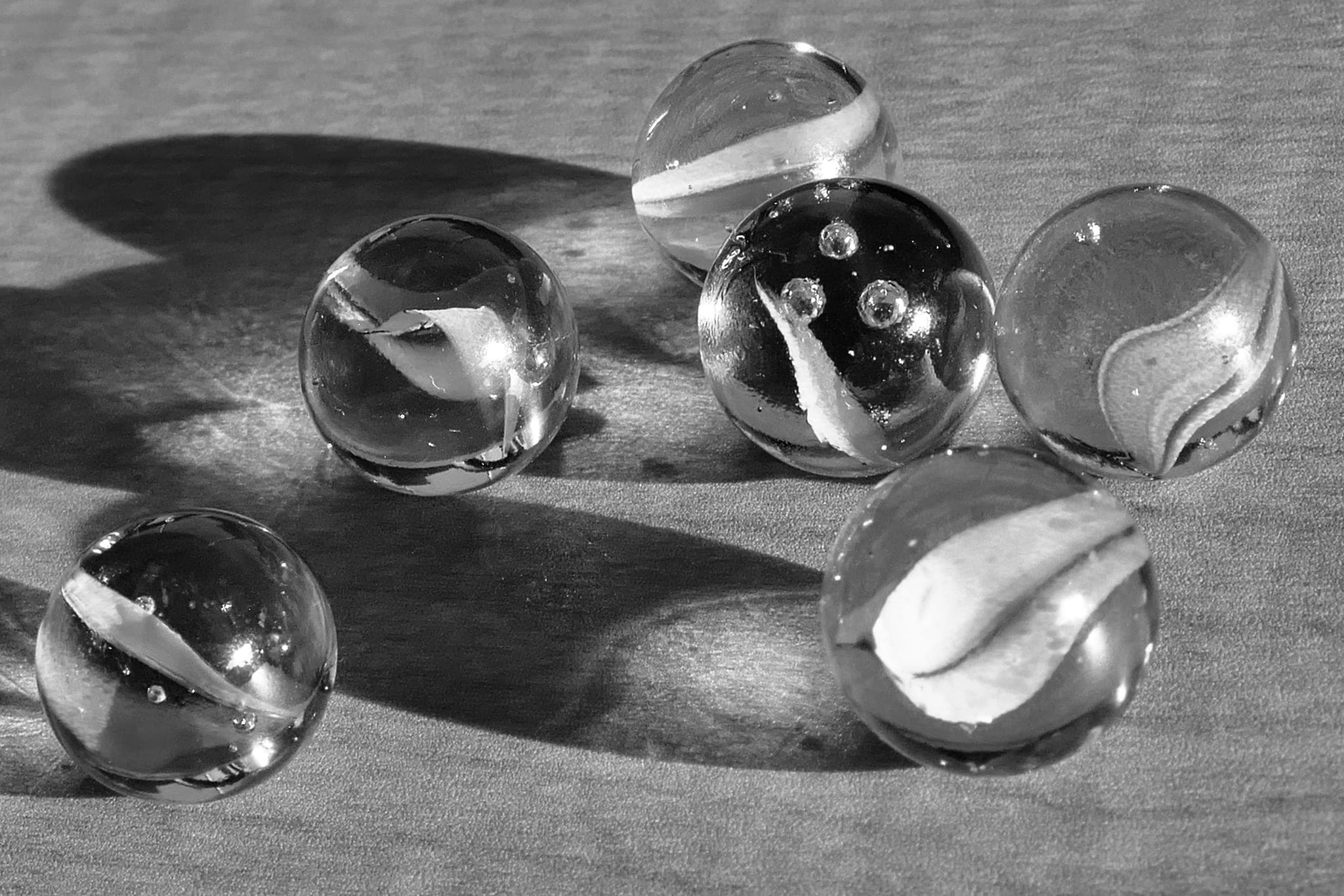Six glass marbles scattered on a wooden surface, each with a different swirl, casting long shadows
