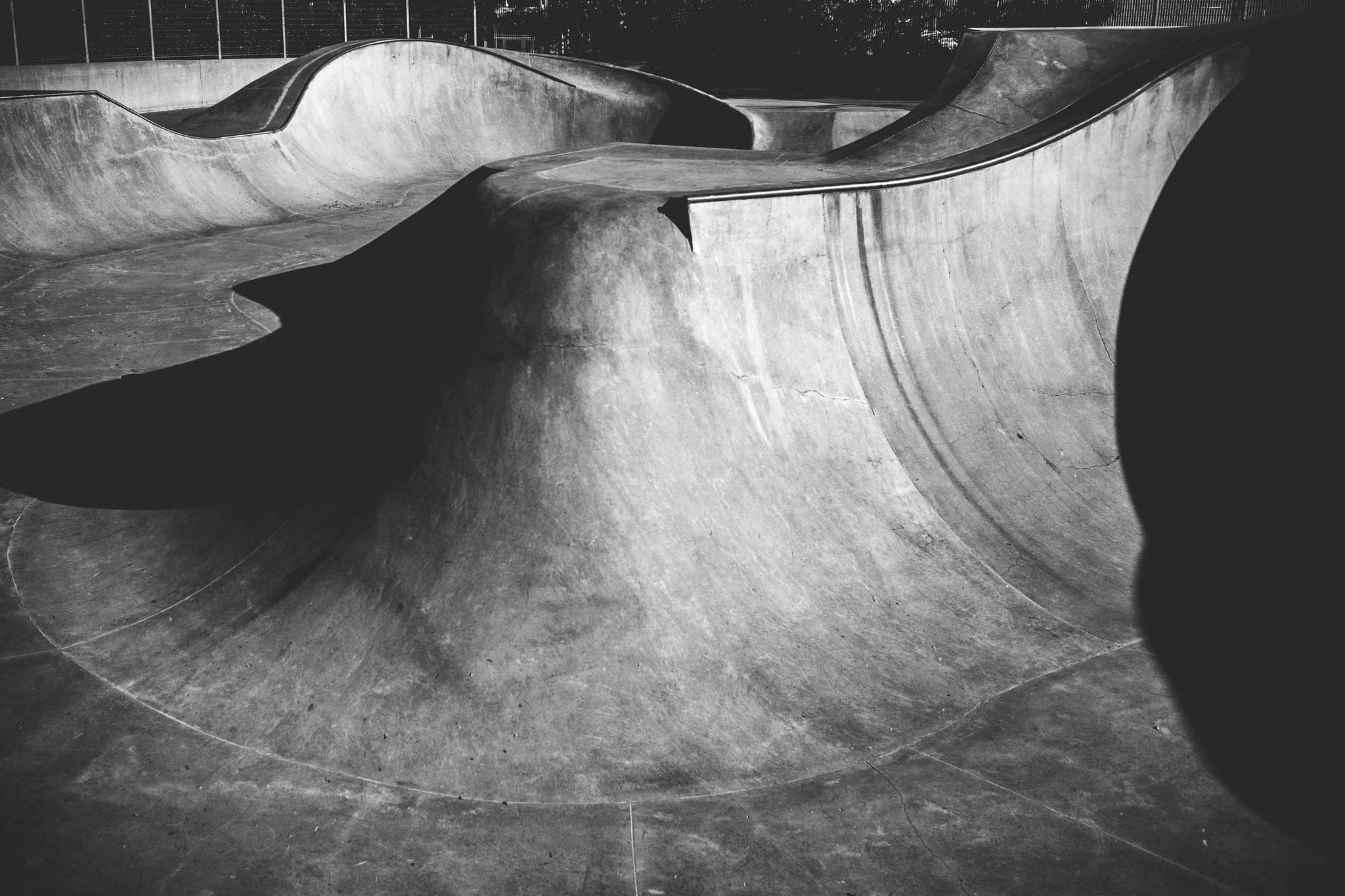 An empty concrete skatepark bowl, its curved walls lit from one side