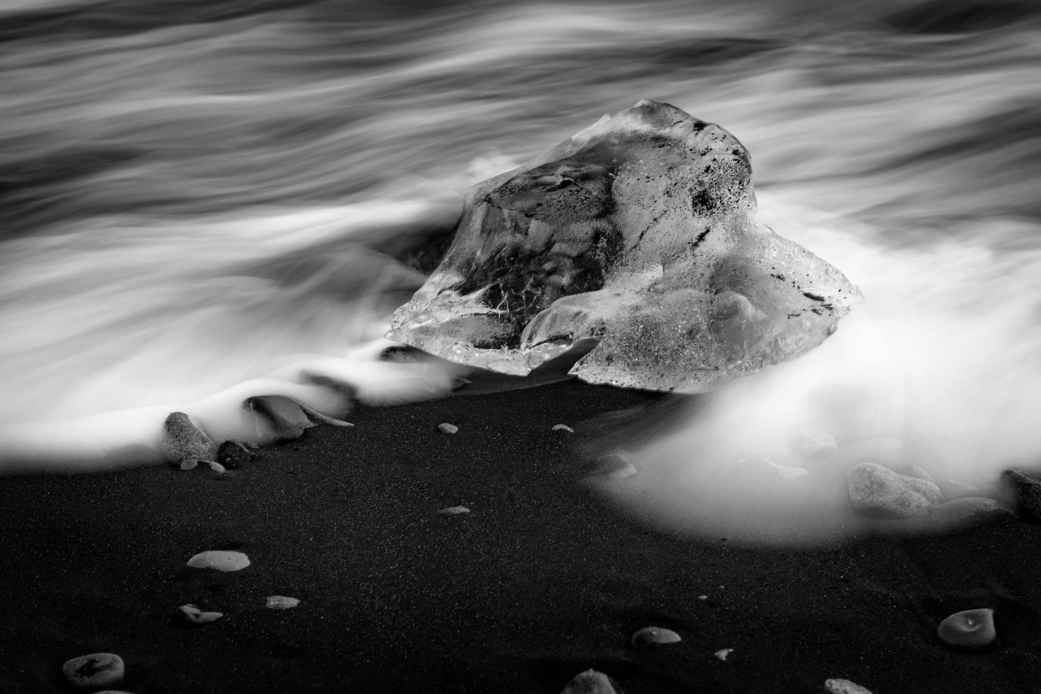 A block of ice on a black sand beach, a long-exposure wave washing around it