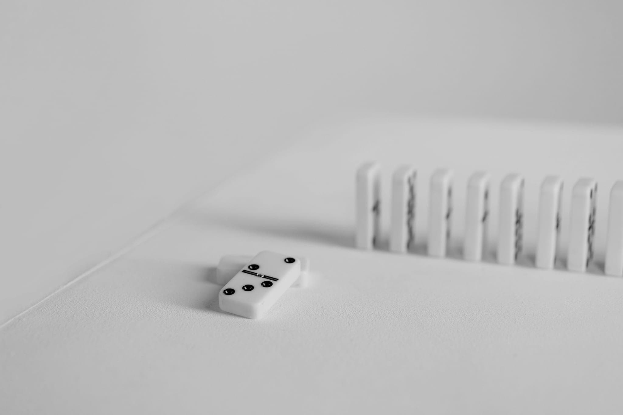 A single domino lying flat in front of a row of standing dominoes on a pale surface