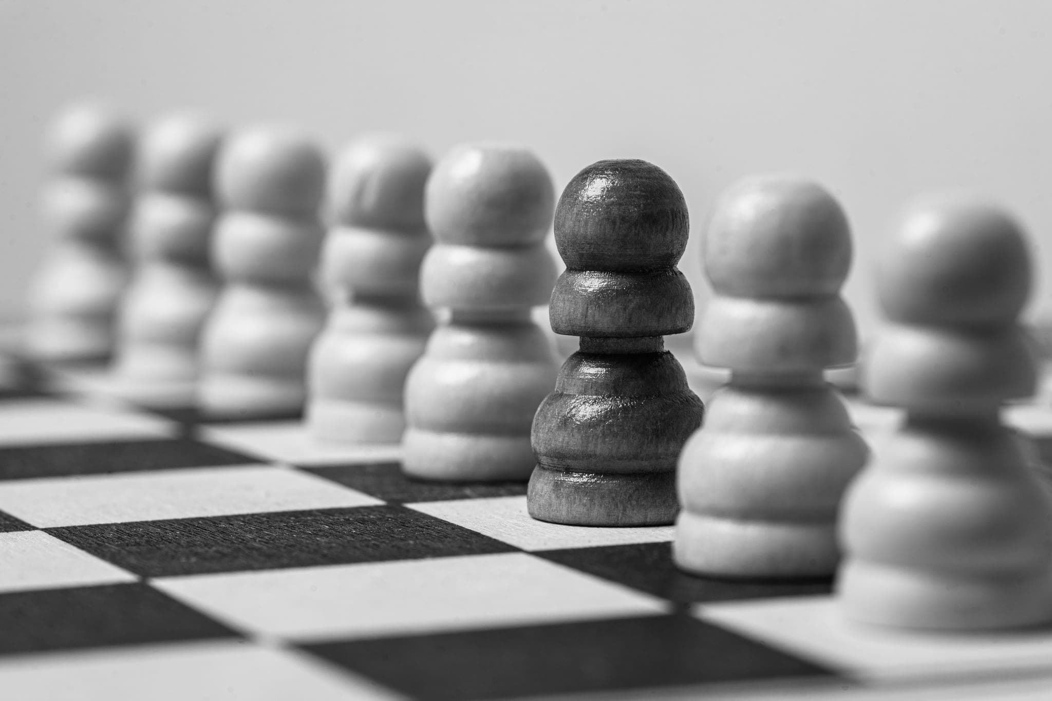 A row of light wooden chess pawns with a single dark pawn among them.