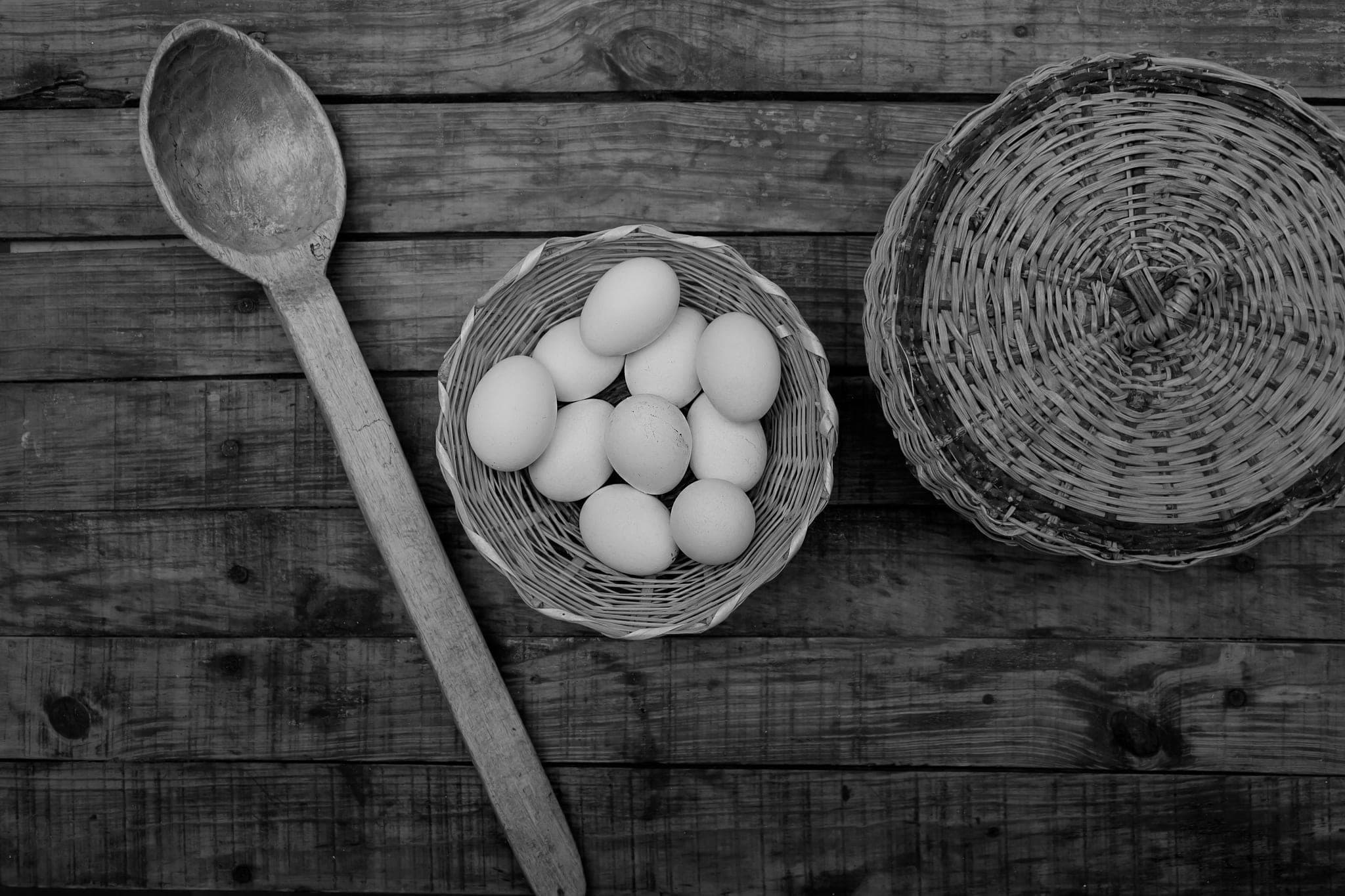 Một giỏ trứng nhỏ trên mặt bàn gỗ, cạnh một chiếc muỗng gỗ và một chiếc giỏ đan khác