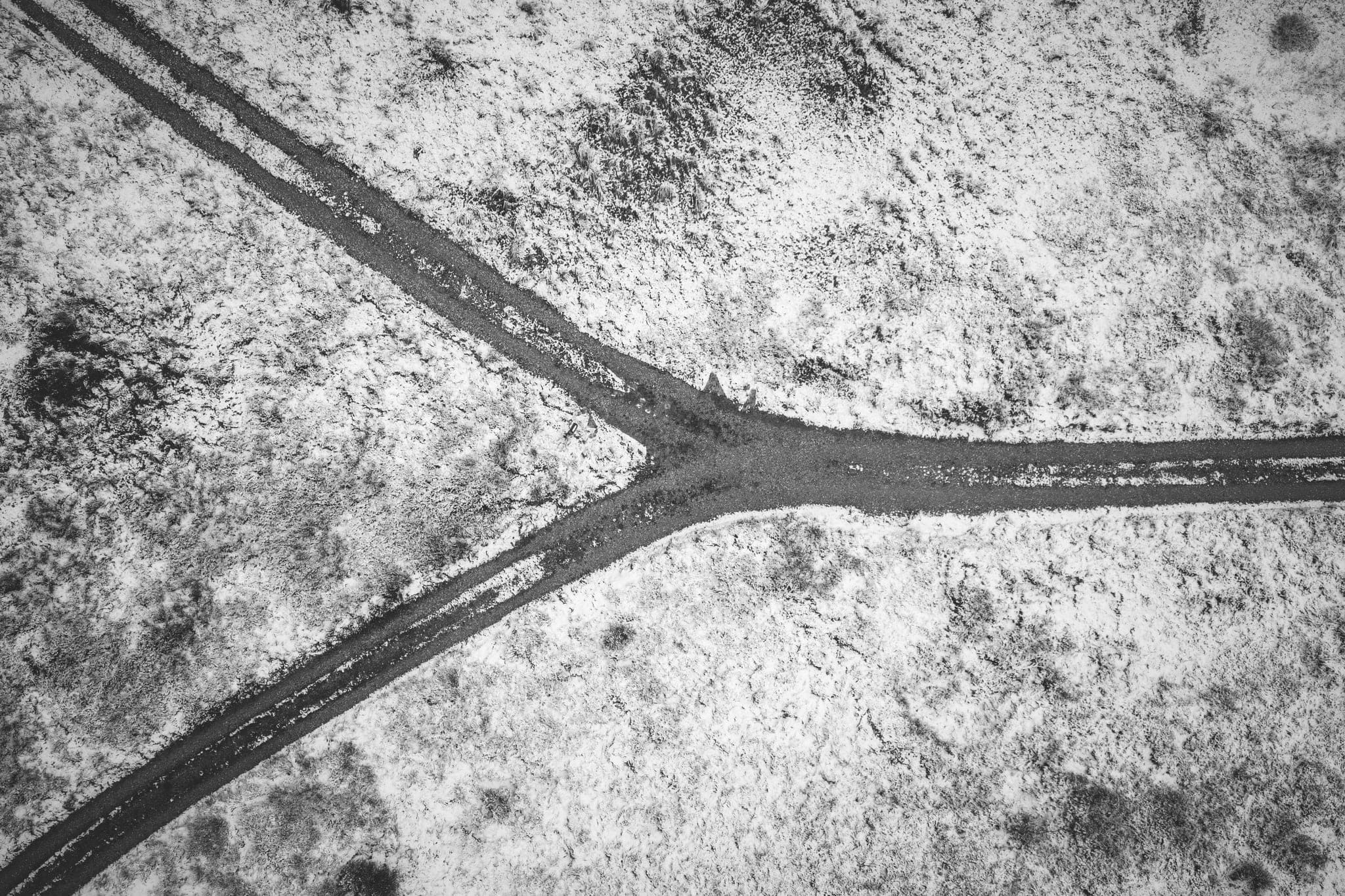 Seen from above, a dirt track splitting in two across snowy ground
