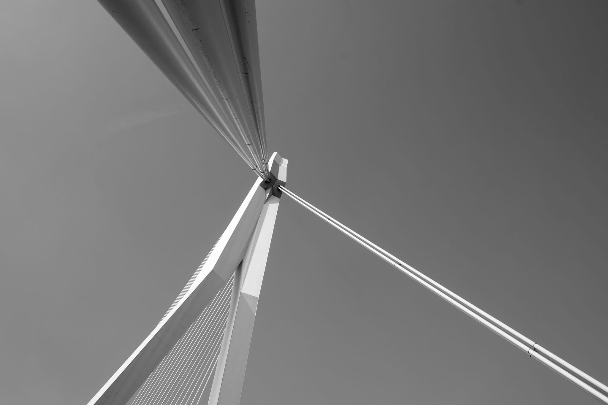 Looking up at a bridge pylon, its cables meeting at a single point against a plain sky