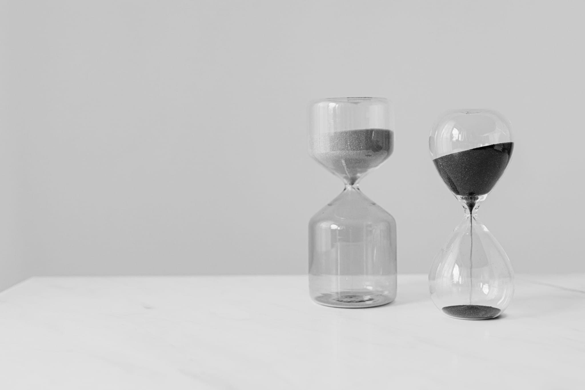 Hai chiếc đồng hồ cát khác dáng đứng cạnh nhau trên mặt bàn sáng màu