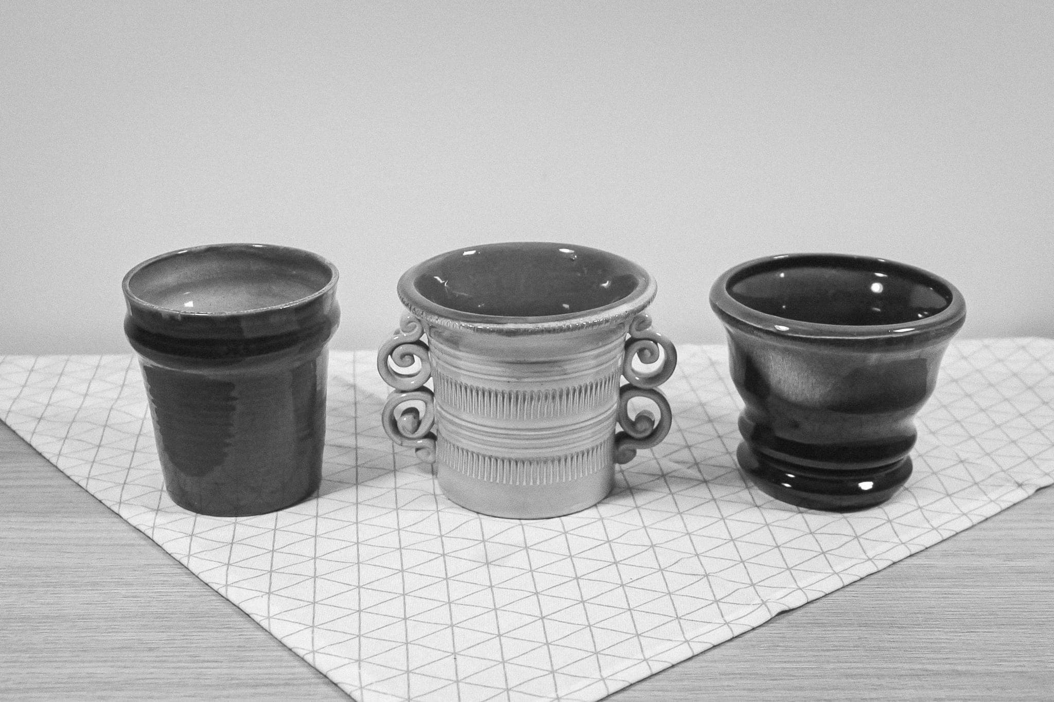 Three ceramic cups of different shapes standing side by side on a patterned cloth