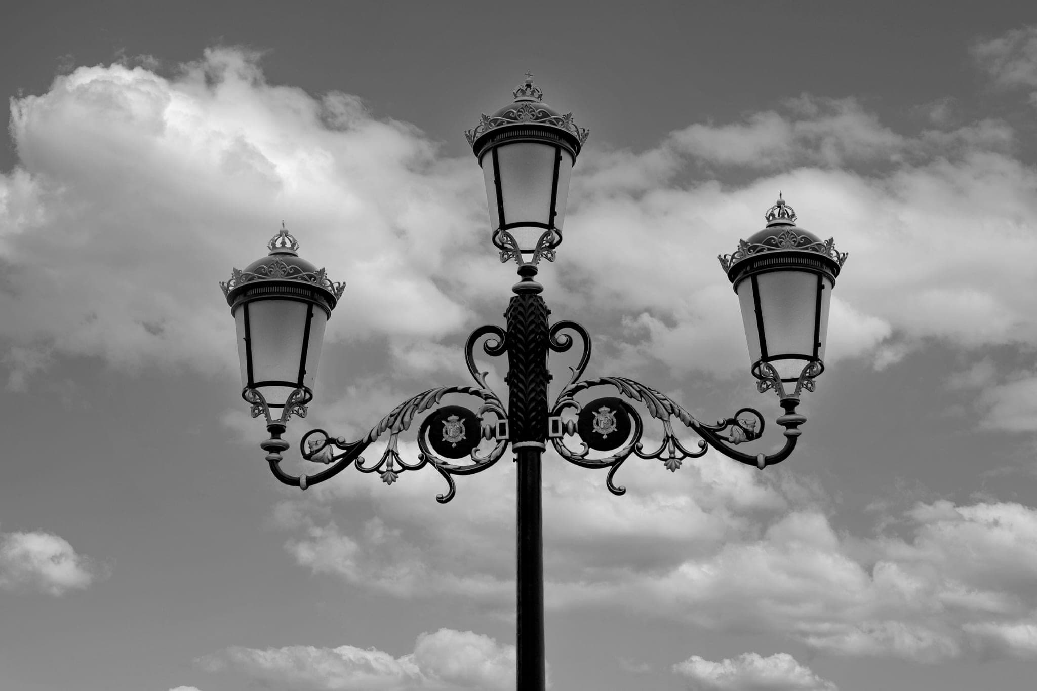 An ornate street lamp with three lanterns against a cloudy sky