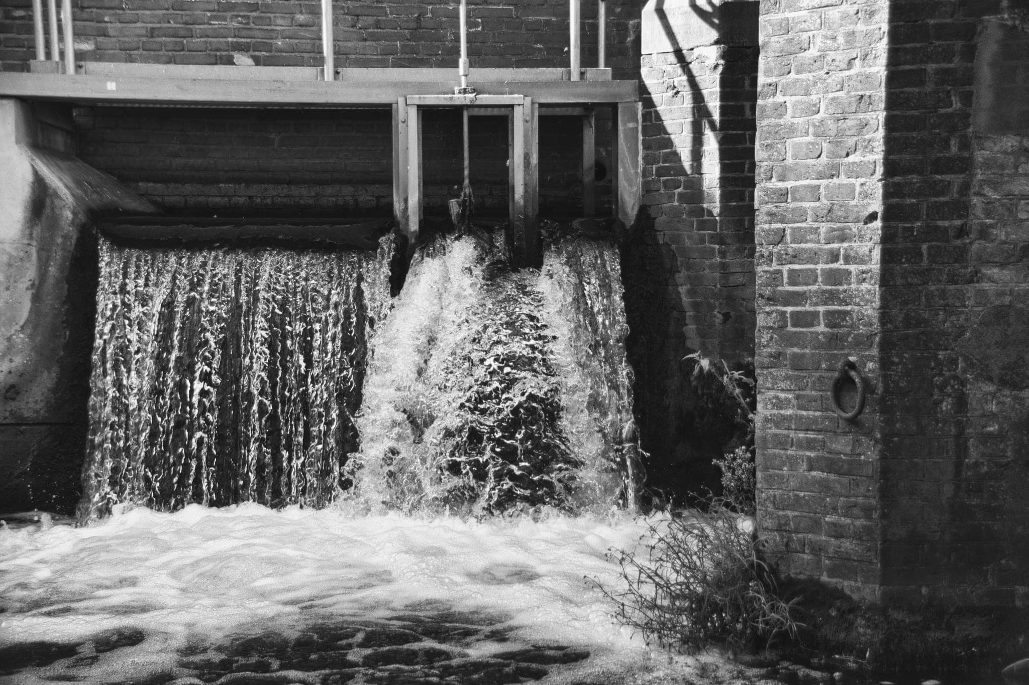 Water pouring through a sluice gate in a brick channel, one section of the gate raised