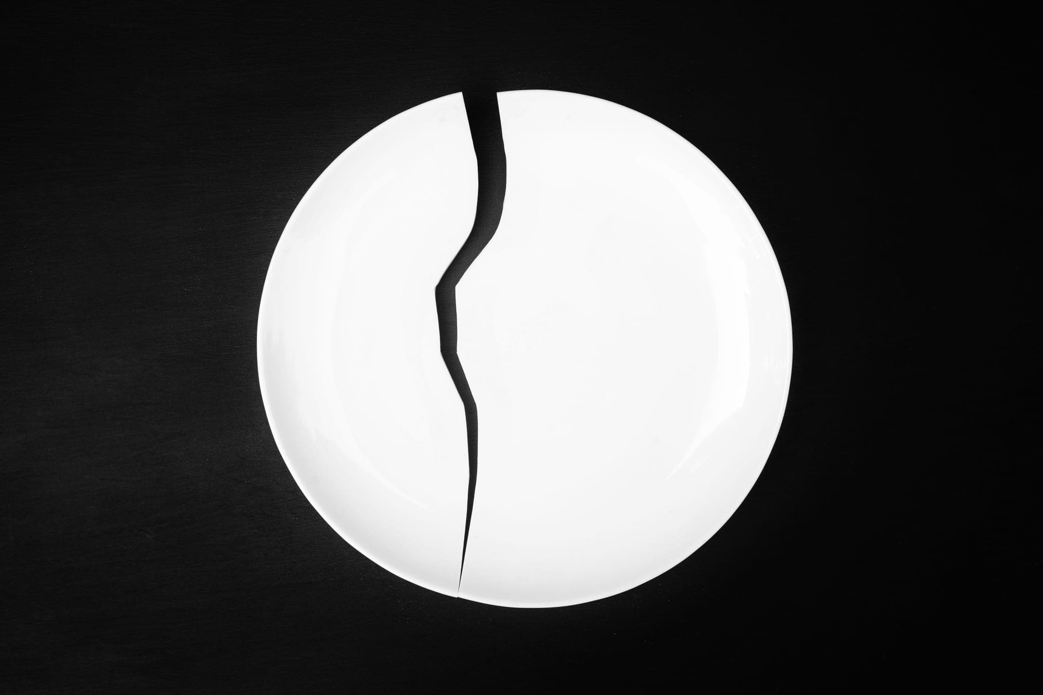 A white porcelain plate with a single crack running across it, on a black ground