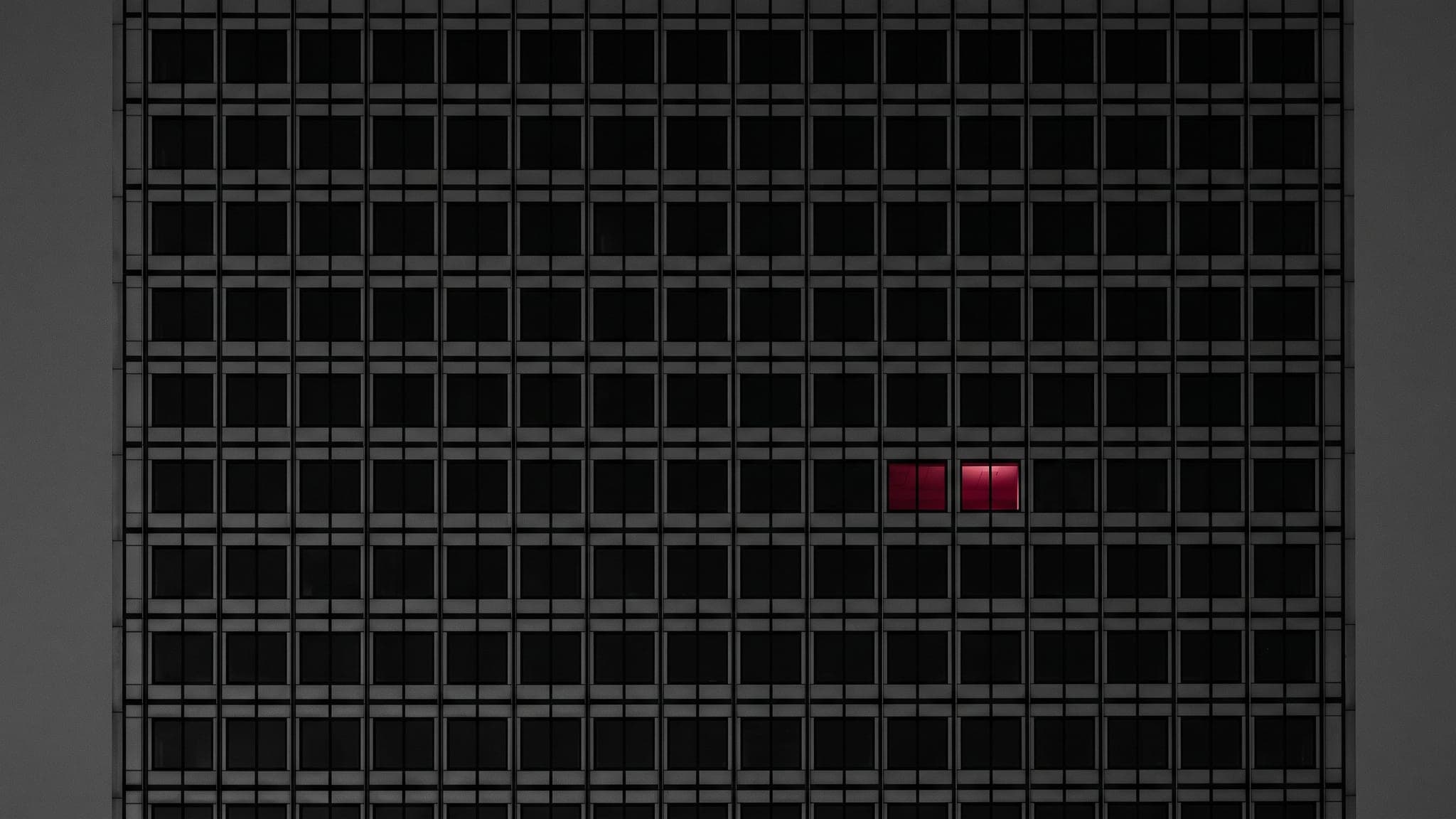 An office tower at dusk with exactly one window lit crimson
