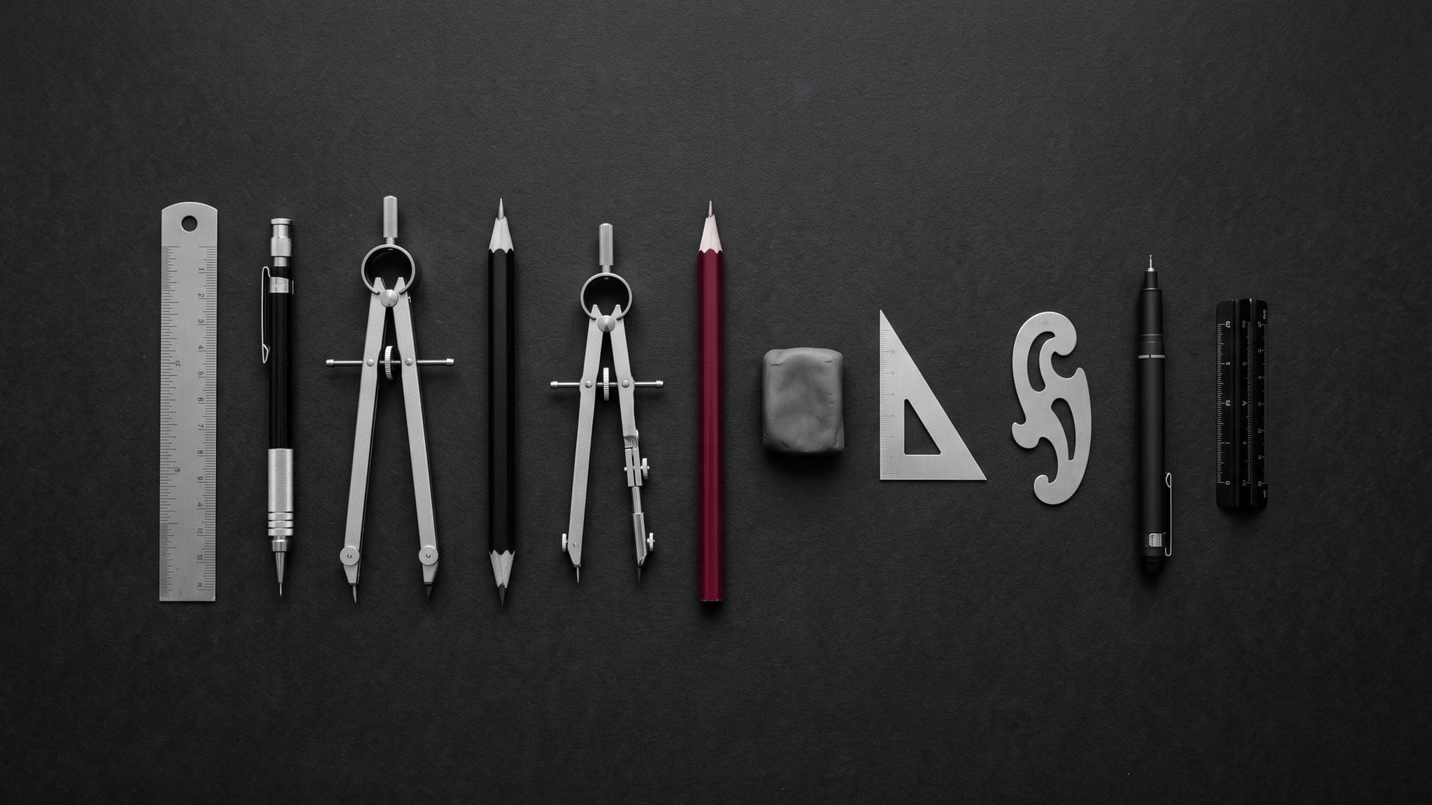 Drafting tools in a row with one crimson pencil