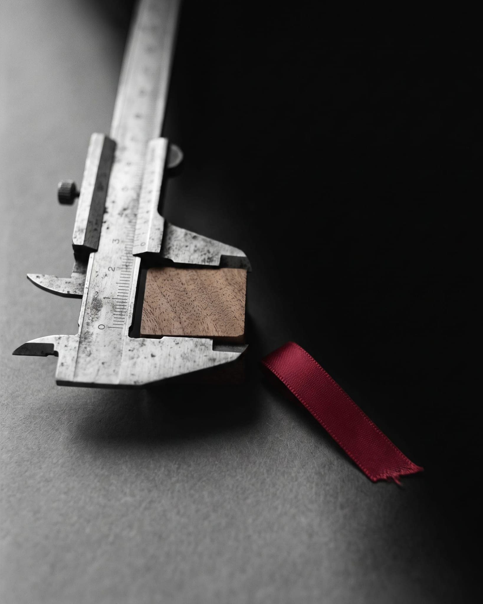 Steel calipers measuring a wooden block, a crimson ribbon beside