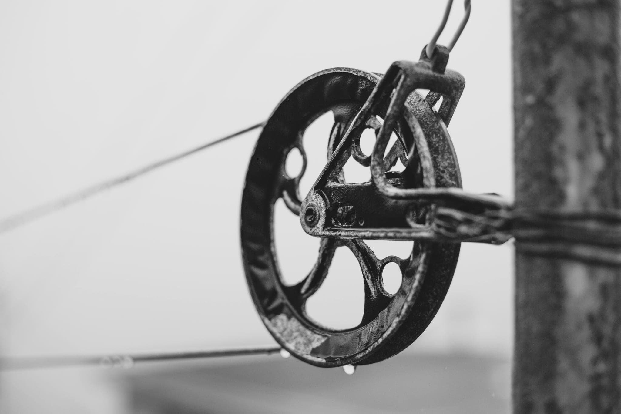 A rusted iron pulley wheel fixed to a post, with a taut line running through it