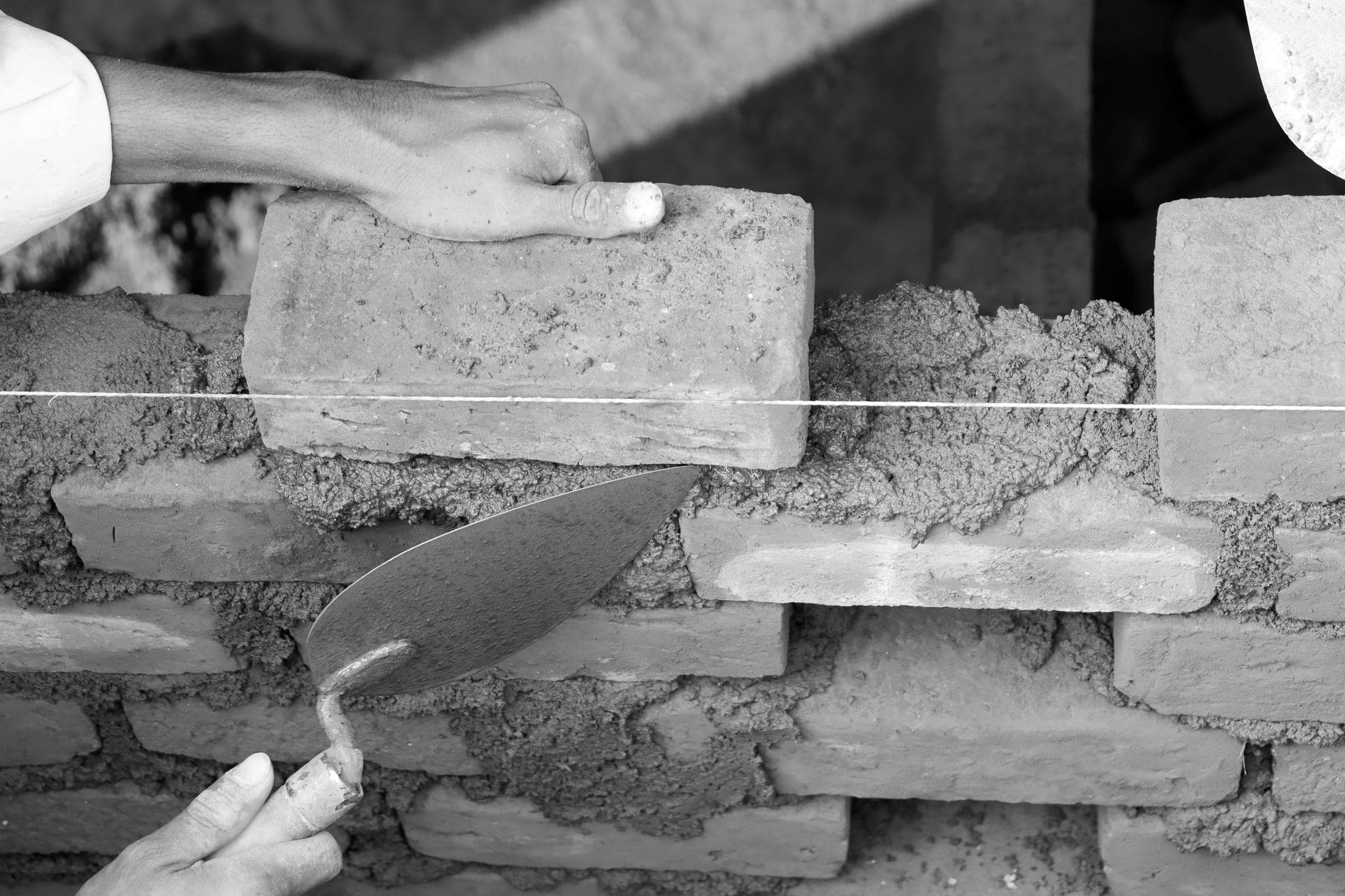 Hai bàn tay đặt viên gạch theo sợi dây căng dọc bức tường đang xây dở