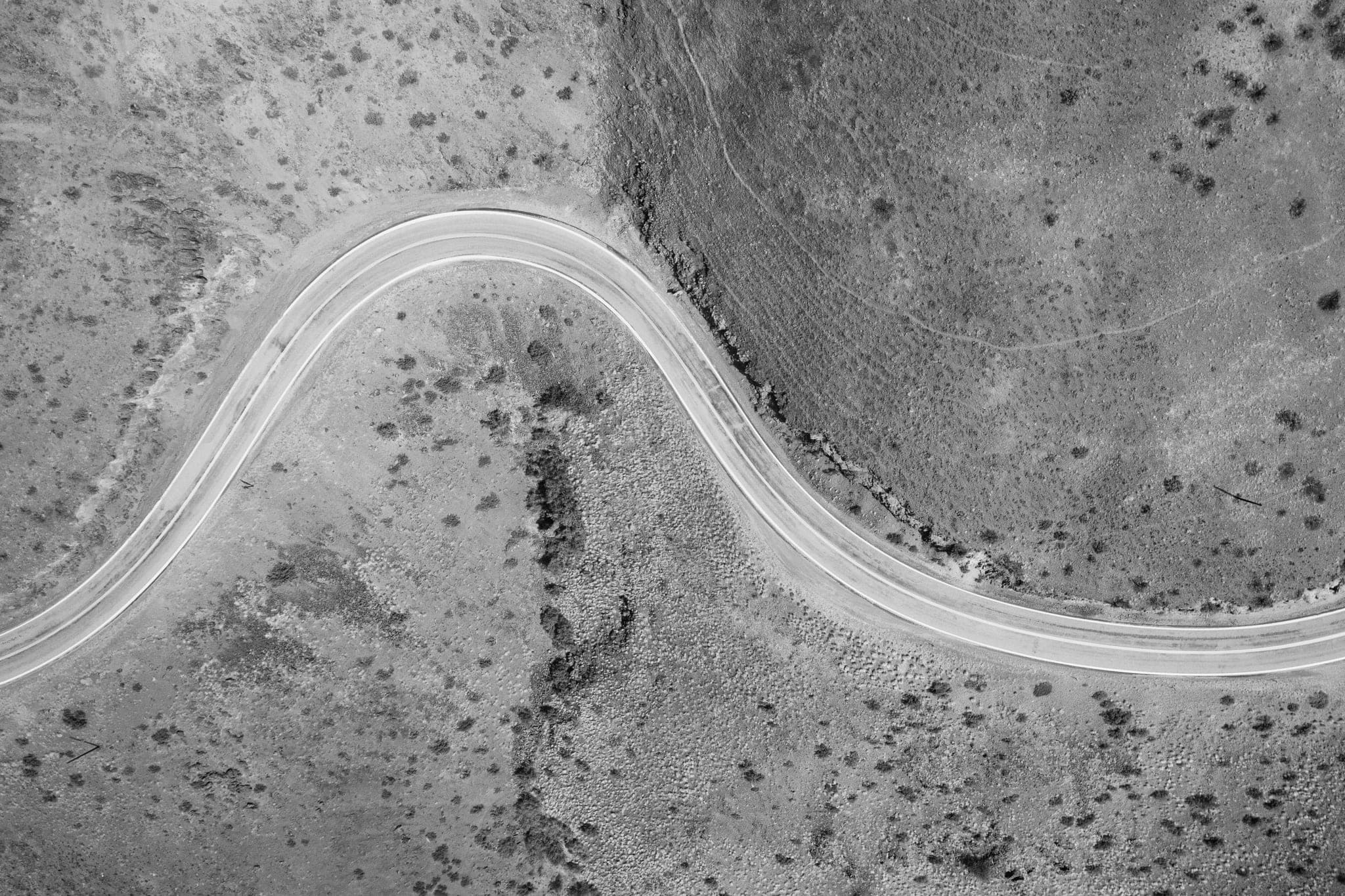 Aerial view of a single road bending through dry, scrubby ground