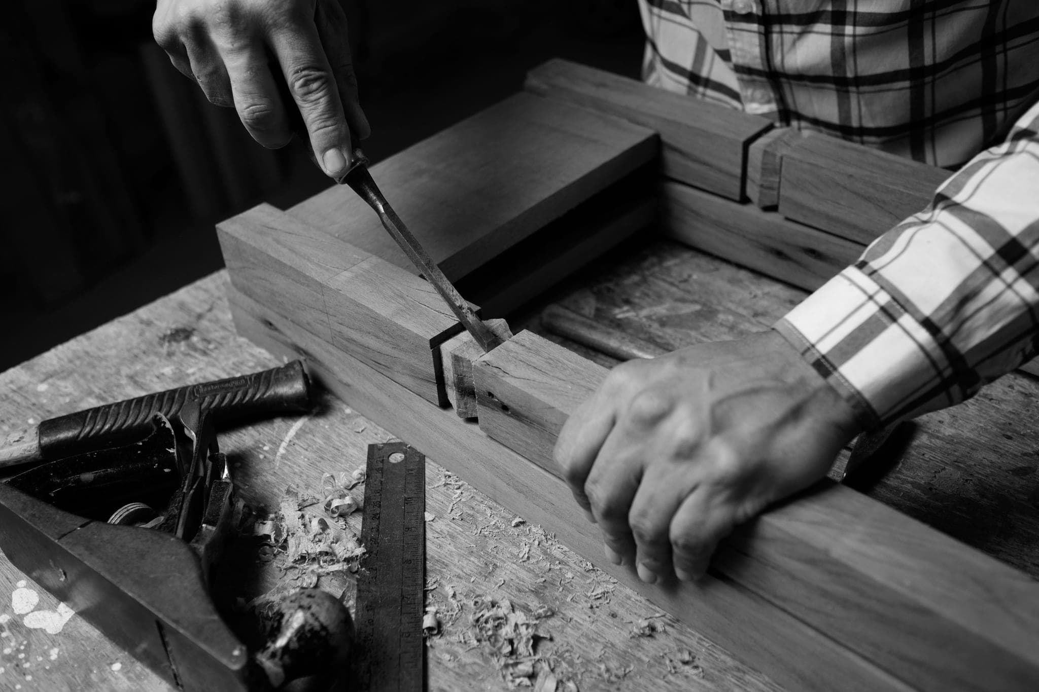 Hands cutting a joint into a timber beam with a chisel, a ruler and a hand plane on the bench