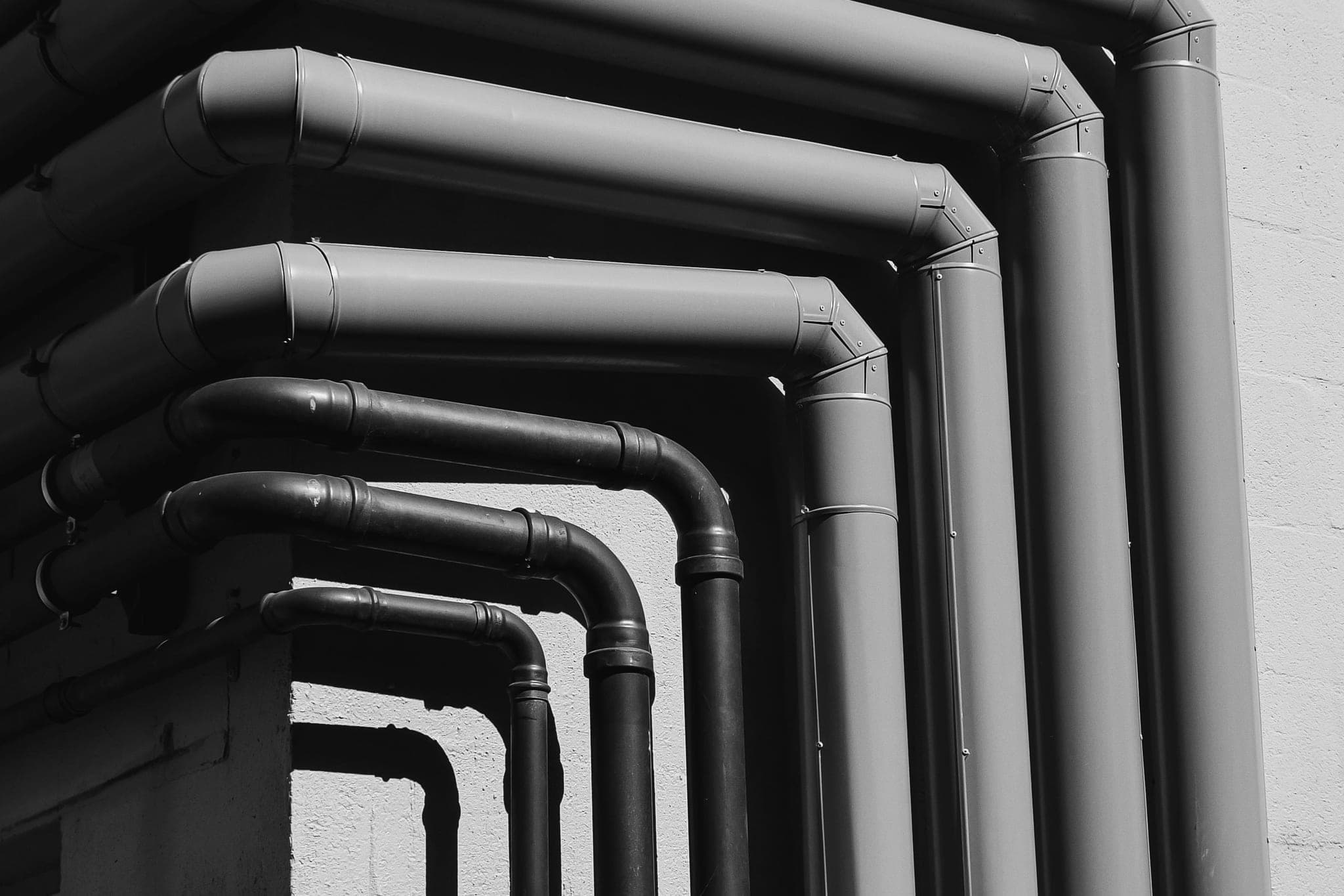 Pipes of different thicknesses bending around a building corner along the same path
