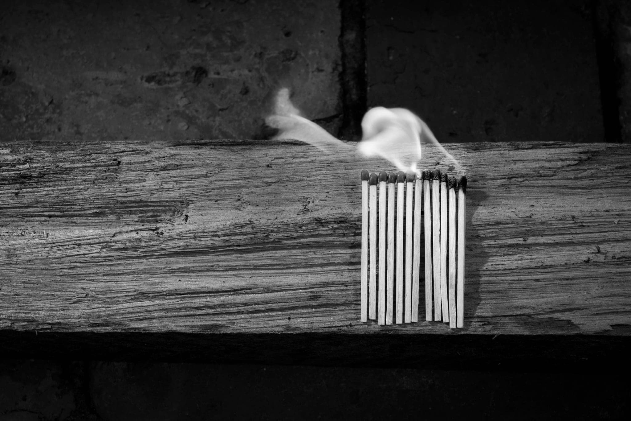 A row of matches on a weathered wooden beam, smoke rising from the heads as they burn