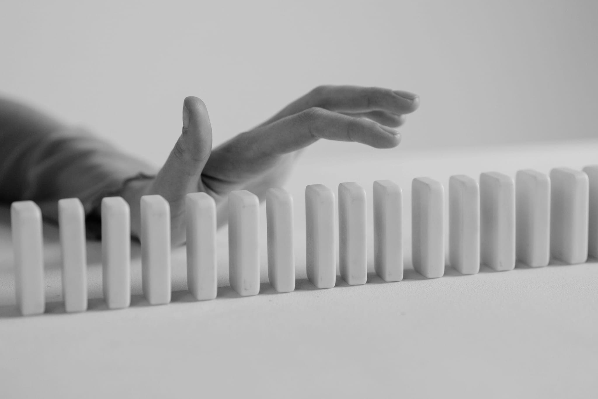A hand held just above a long row of standing dominoes