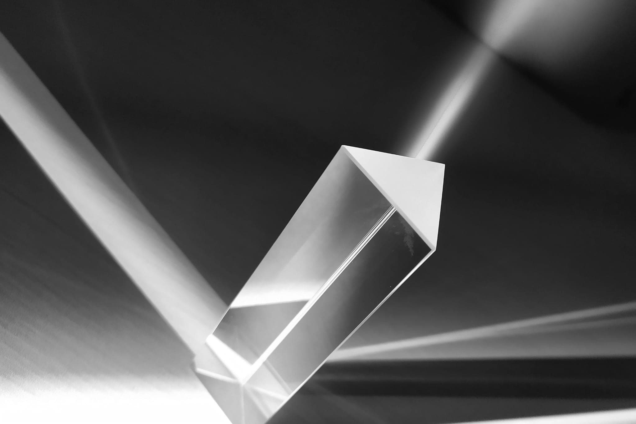 A glass prism on a dark surface, a beam of light passing through it and splitting into several beams