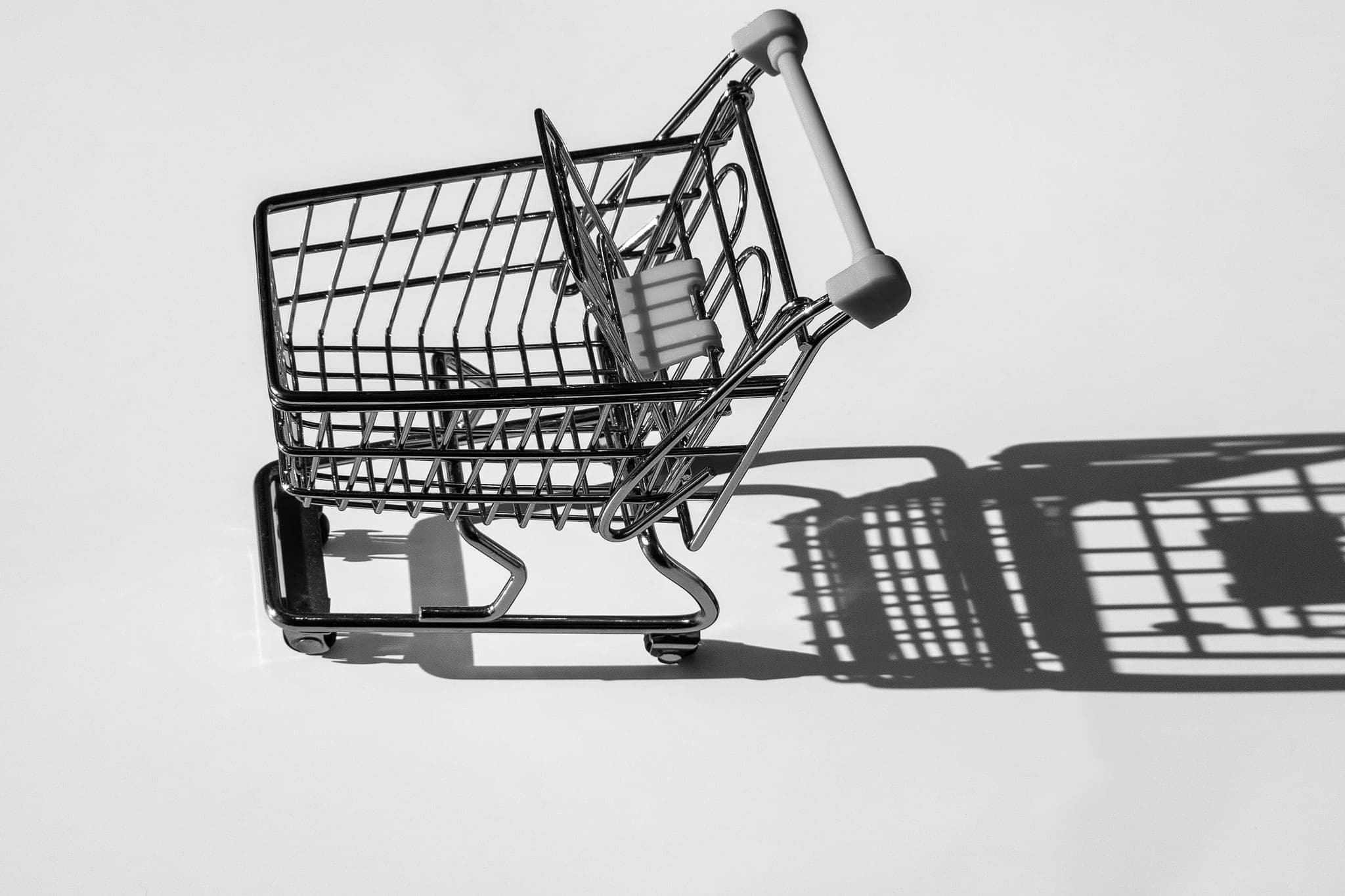 A miniature shopping cart on a white surface, casting a long shadow