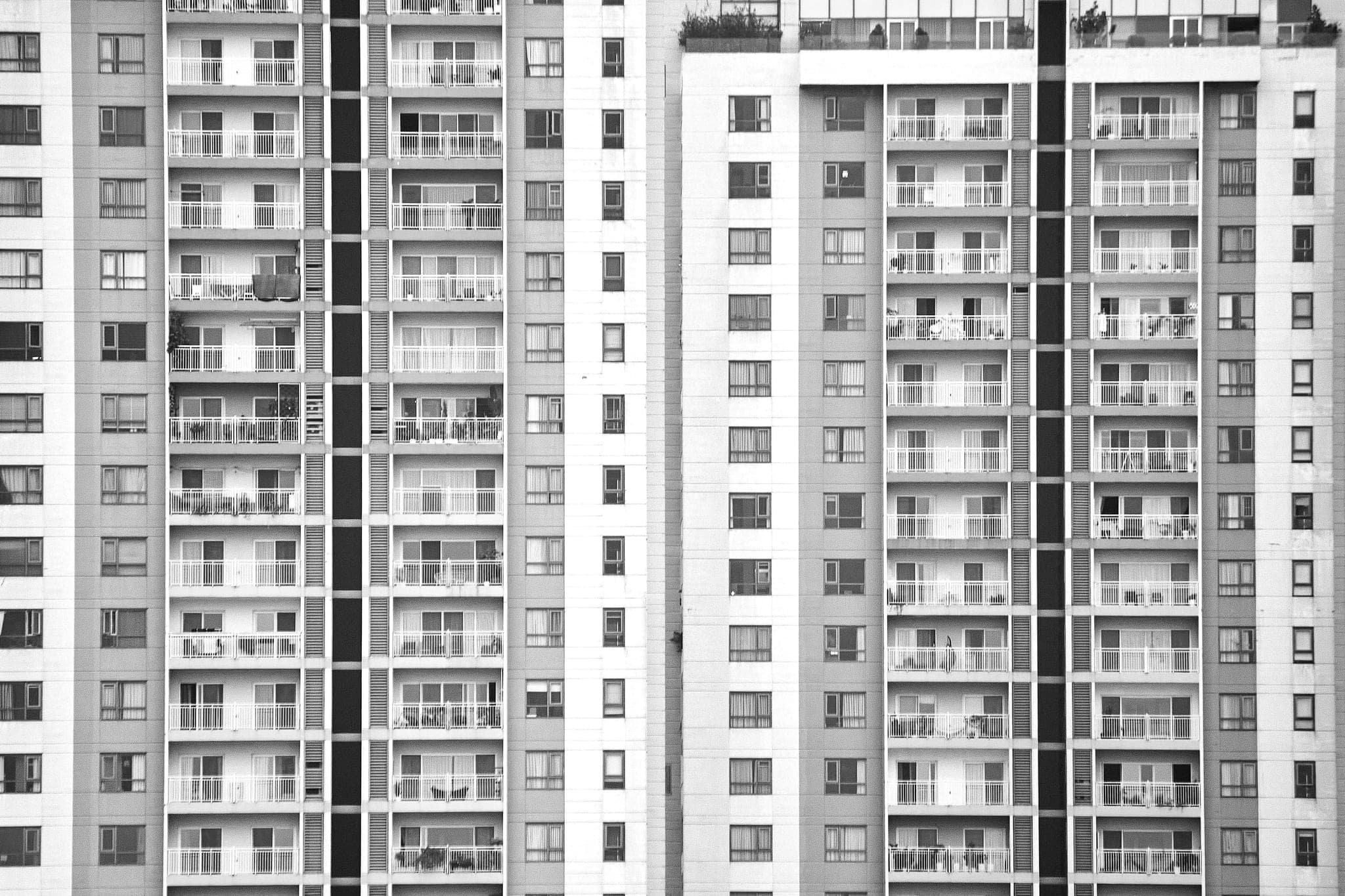 Two white residential towers, rows of balconies with plants and laundry