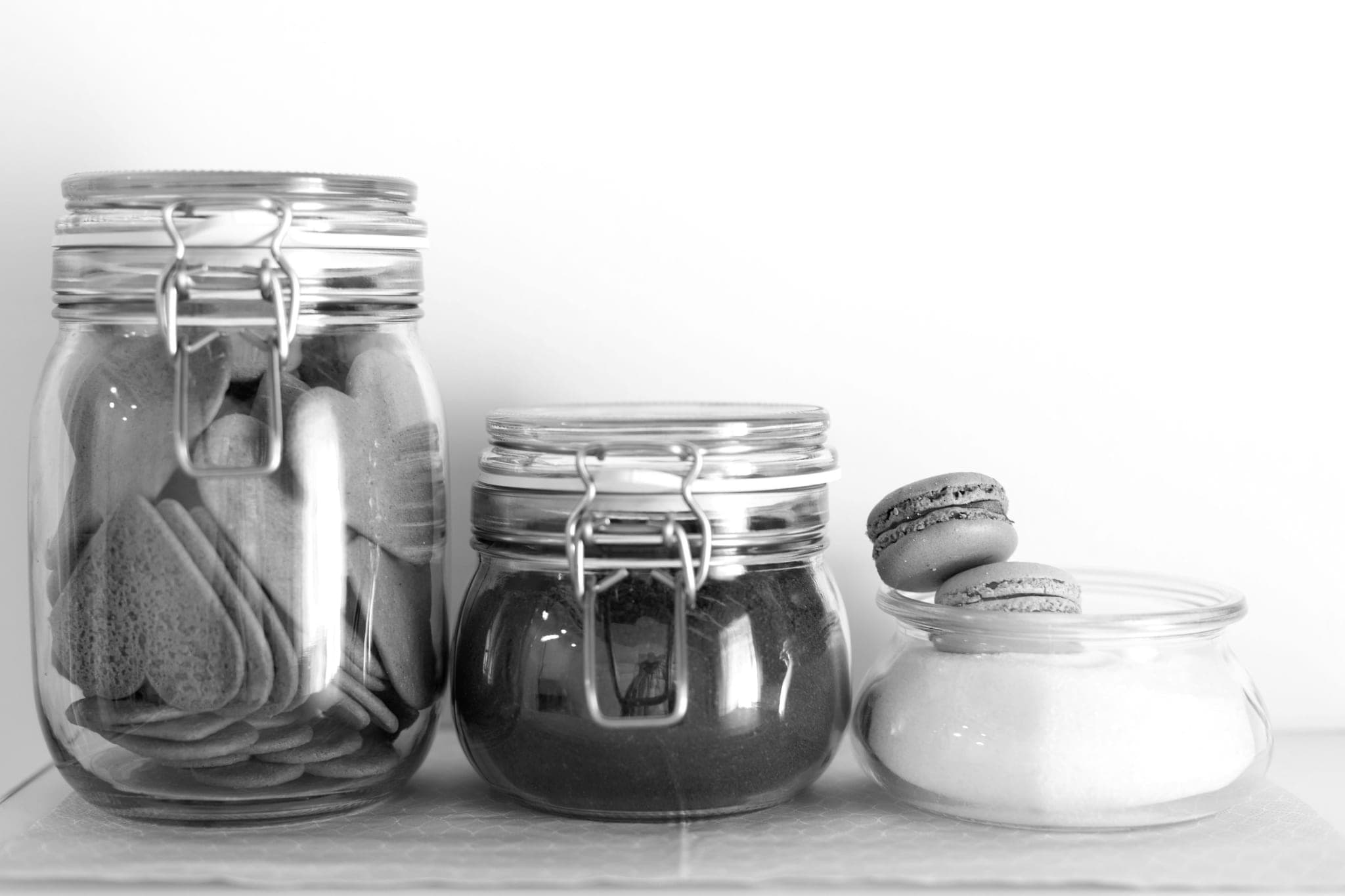 Three glass jars of different sizes on a shelf, holding biscuits and dry goods, two macarons on the smallest
