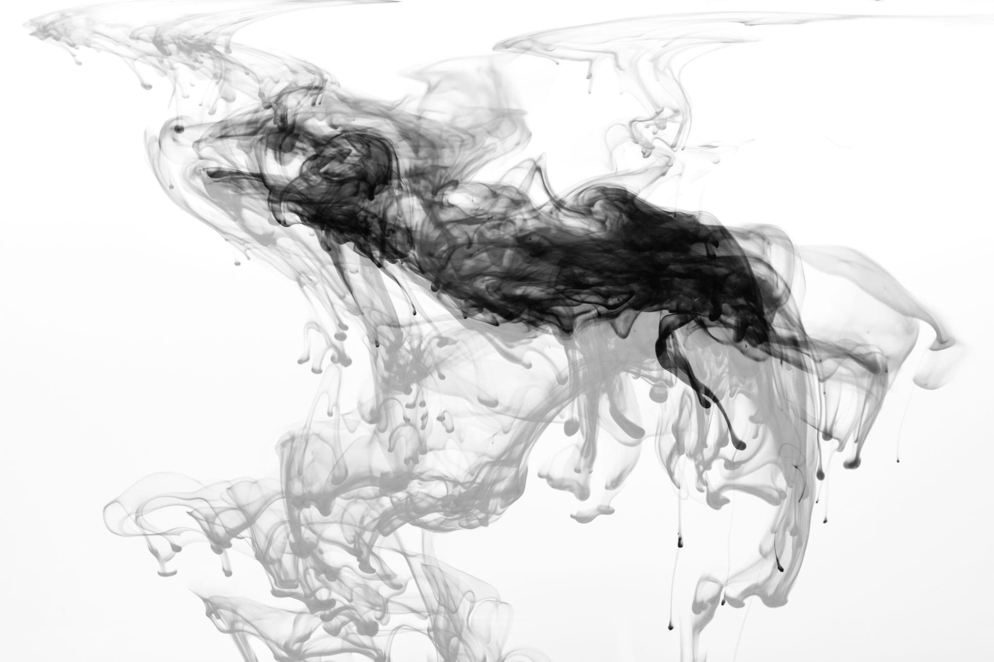 Dark ink spreading through clear water in uneven threads