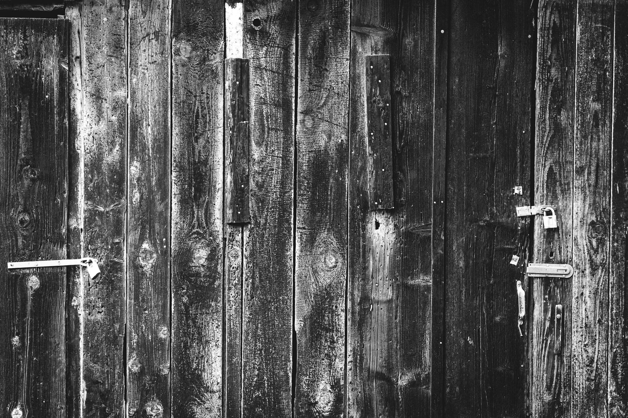 The weathered wood of several old doors, with latches and padlocks