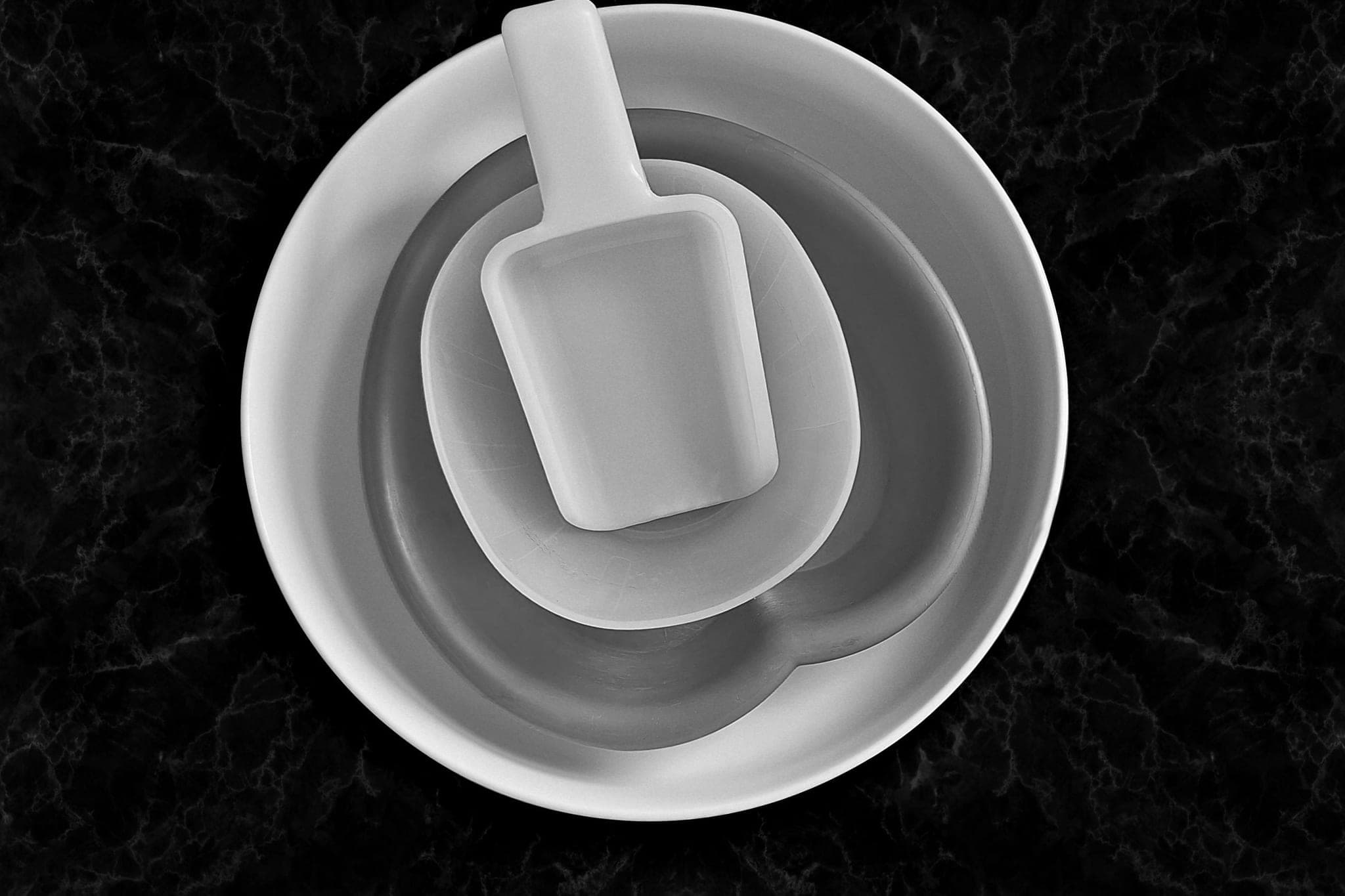 Pale bowls nested one inside another, a small scoop in the innermost, on dark marble