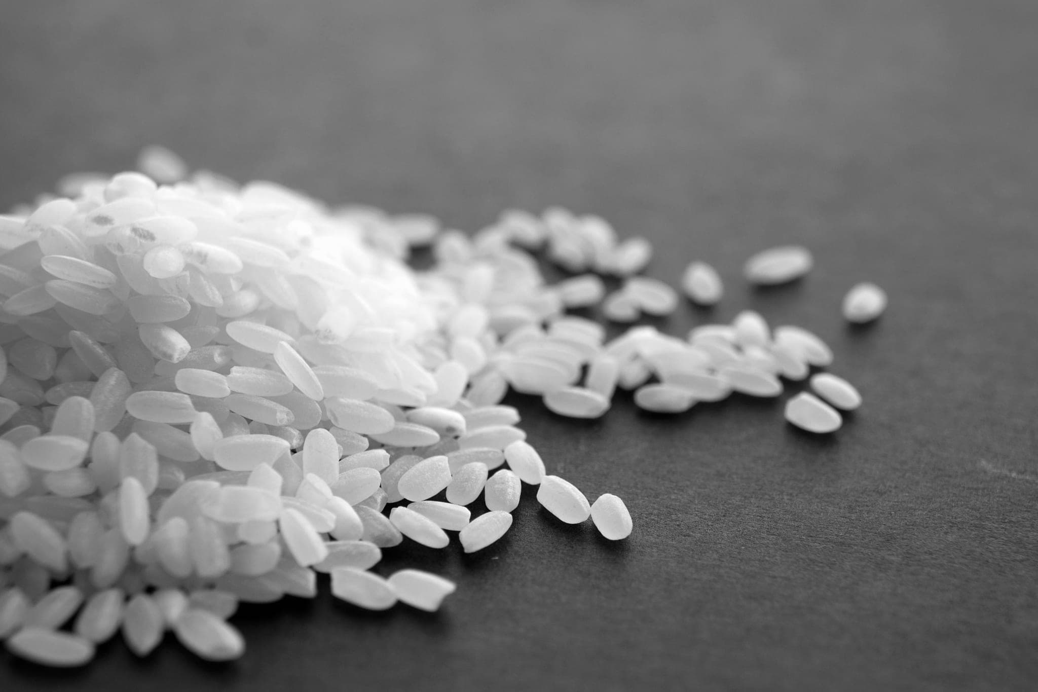 A heap of white rice grains spilling across a dark surface