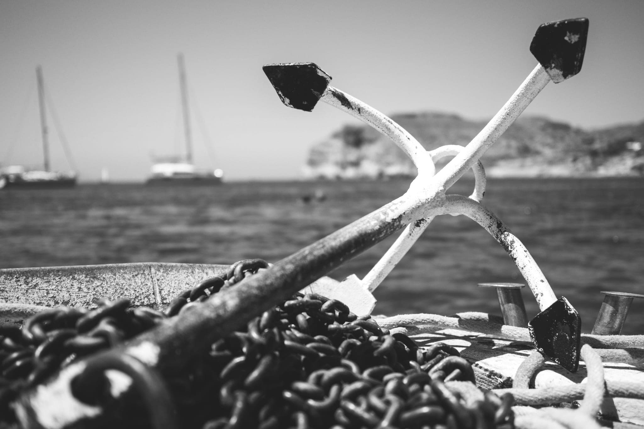 An anchor resting on a coil of chain, water and moored boats behind
