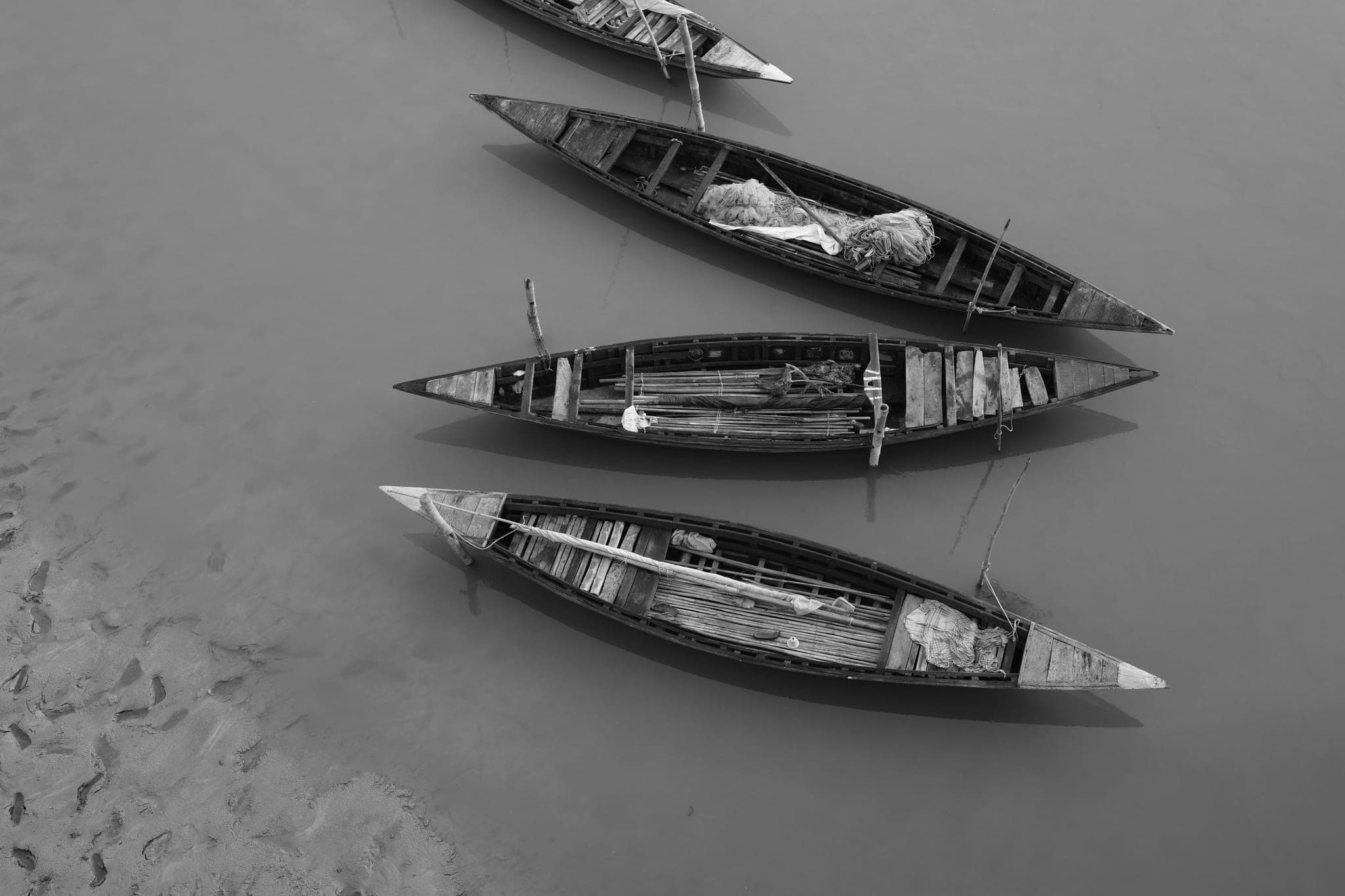 Four wooden boats moored side by side in shallow water, seen from above